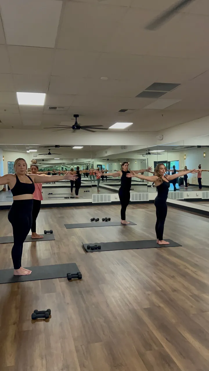 A standing yoga class with the instructor guiding from the mirrored wall