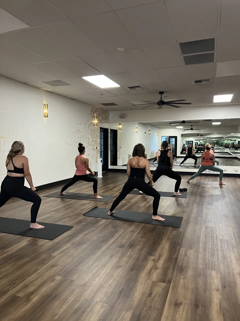 A full hot yoga class flowing together across the mirrored studio floor