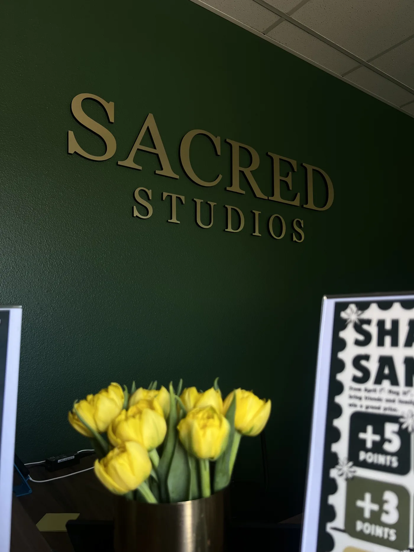 Sacred Studios reception — gold lettering on the deep green wall with fresh tulips